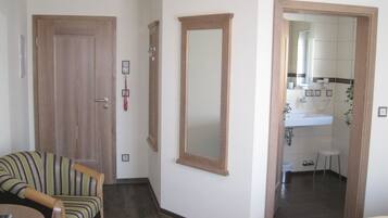 A hotel room with a wooden door, a mirror, a small stool, and a bed.