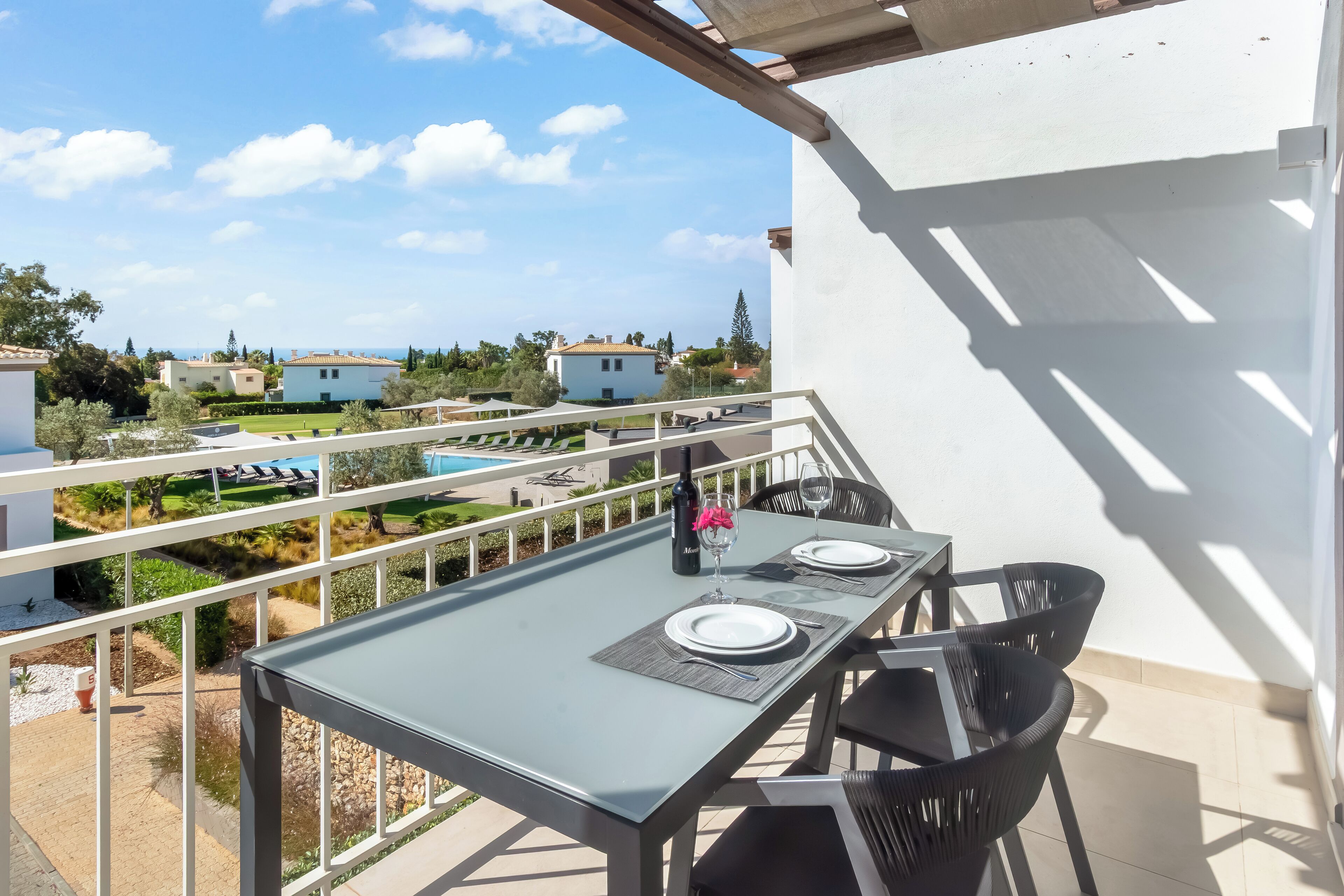 Un balcó amb taula preparada per a dues persones, amb vista a una piscina i edificis residencials.