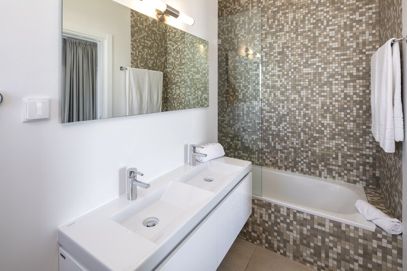 Een moderne badkamer met een witte wastafel, een douche met glazen wanden en mozaïek betegelde muren.