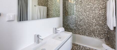 Een moderne badkamer met een witte wastafel, een douche met glazen wanden en mozaïek betegelde muren.
