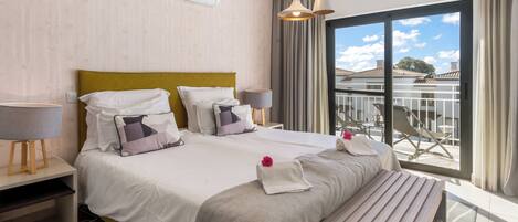 A modern hotel room with a large bed, bedside tables, a bench, and a balcony with a view.