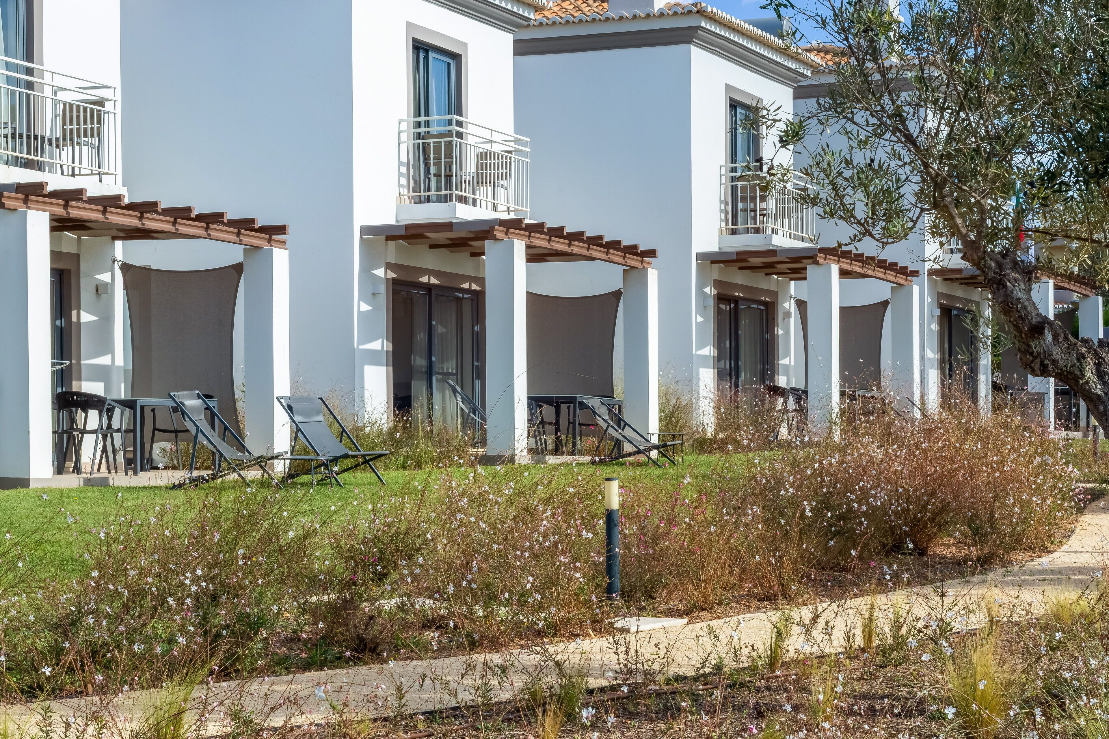 Una hilera de edificios blancos con balcones, mobiliario exterior y un jardín bien cuidado.