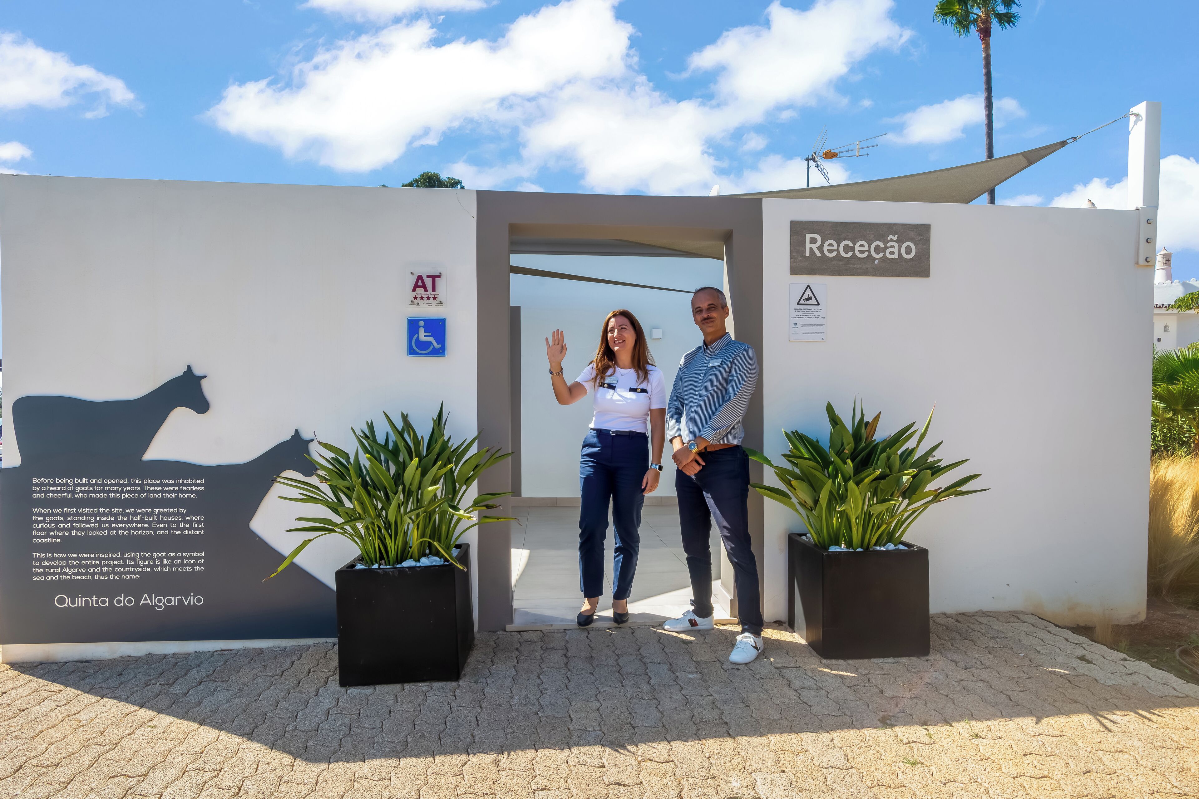 Un espace d’accueil avec une enseigne indiquant « Receção » et la silhouette d’une chèvre peinte sur le mur. On y trouve deux plantes en pot et un panneau indiquant l’accessibilité pour les personnes en fauteuil roulant.