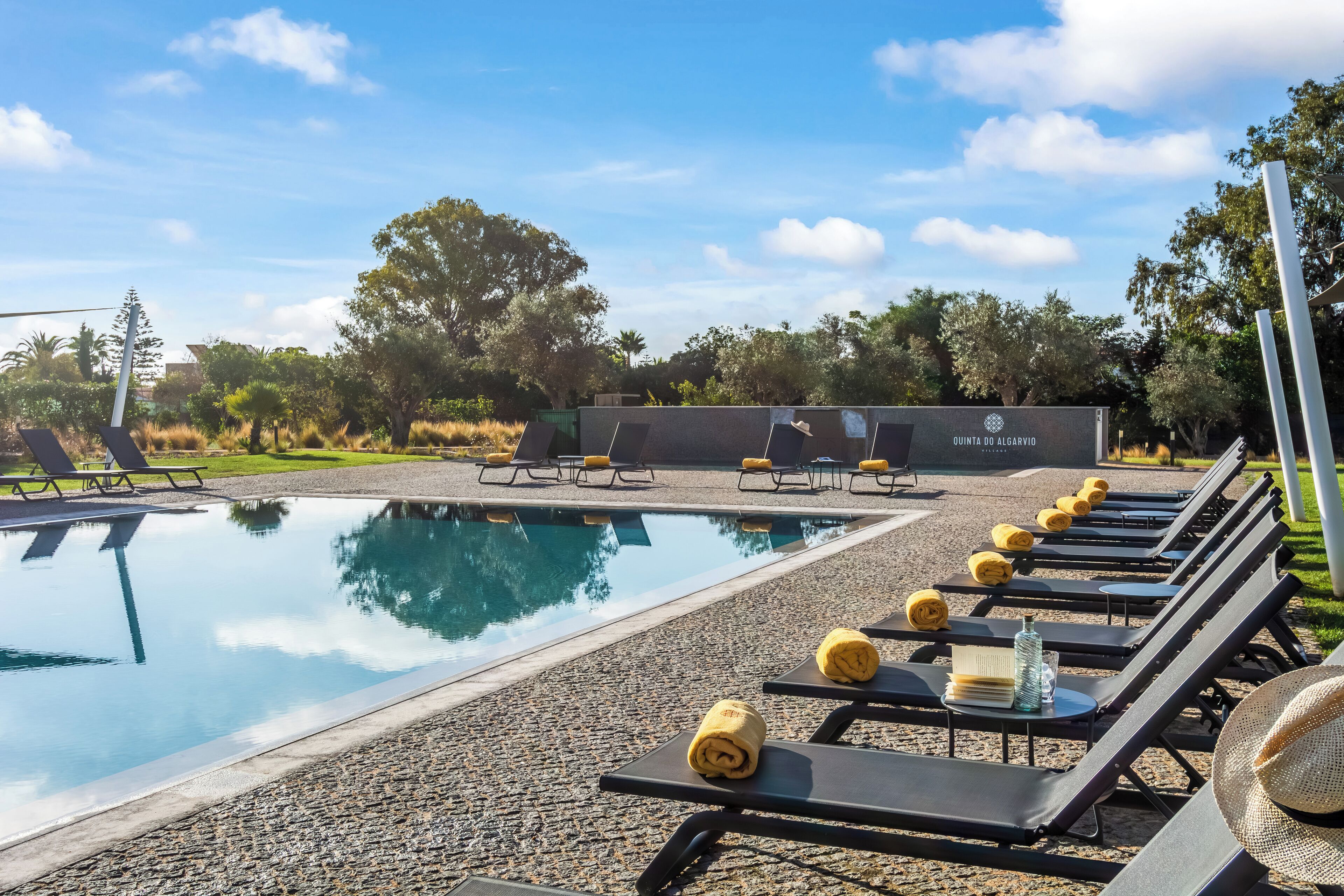 A poolside area with lounge chairs, a pool, and a building labeled 'QUINTA DO ALGARVIO VILLAGE'.