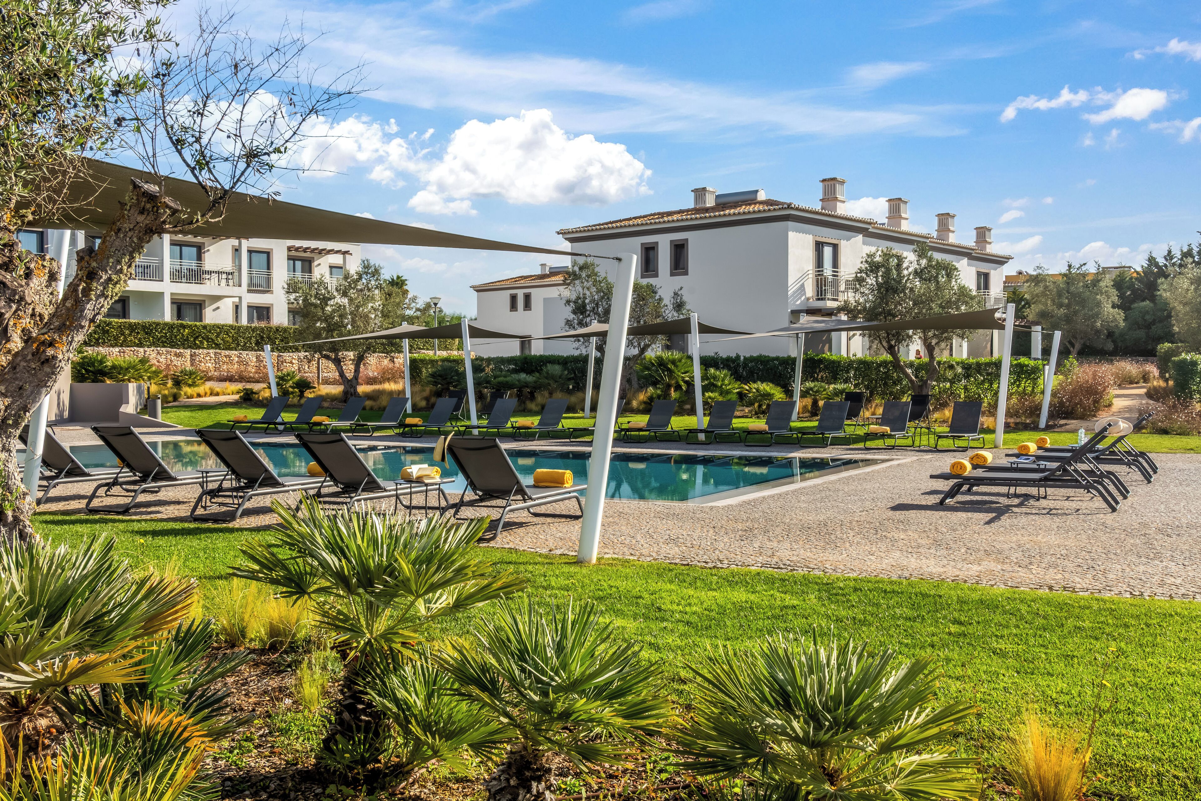 A poolside area with sun loungers, a pool, and a building with balconies.