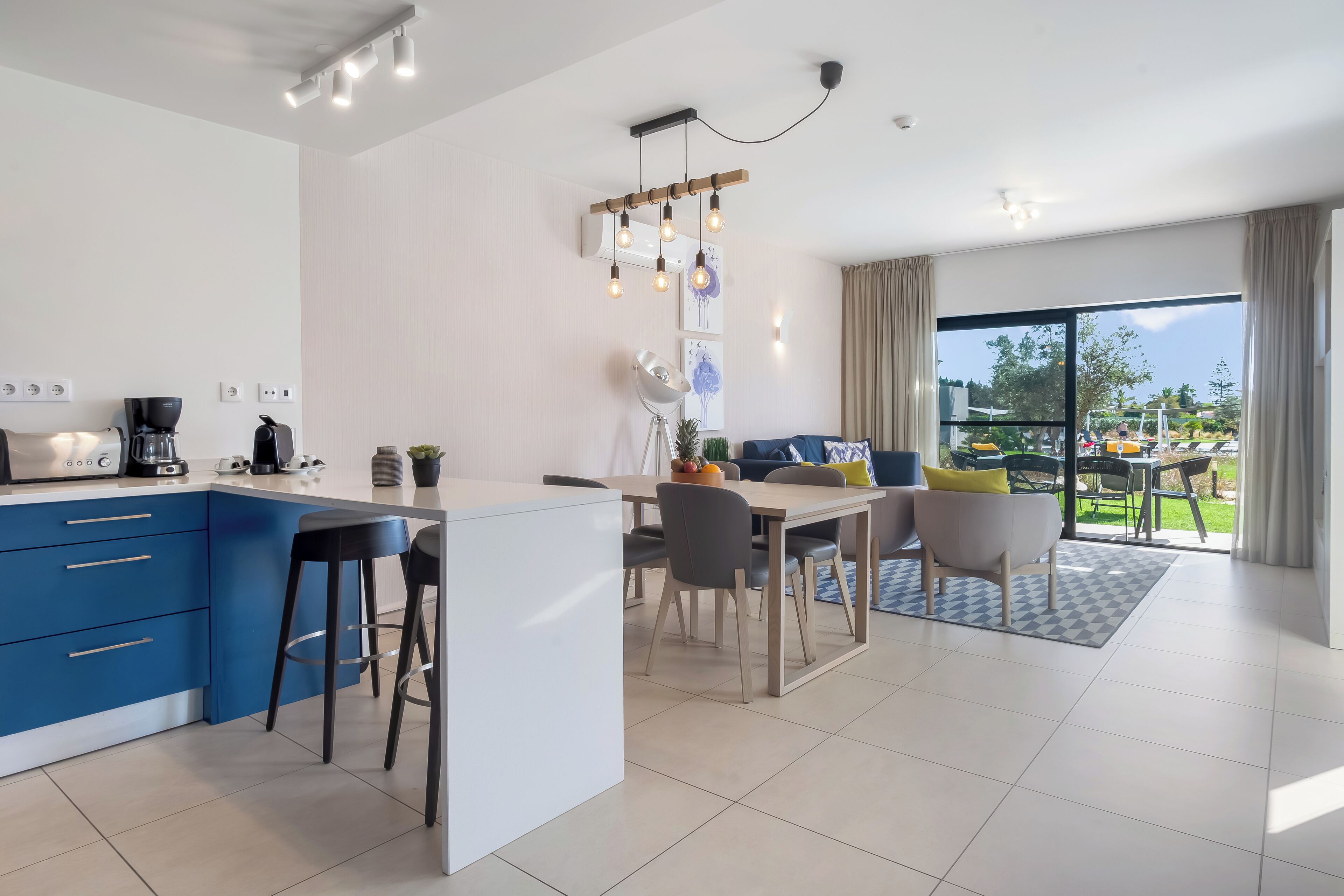 A modern kitchen with blue cabinets, a dining area with a table and chairs, and a large sliding glass door leading to a balcony.