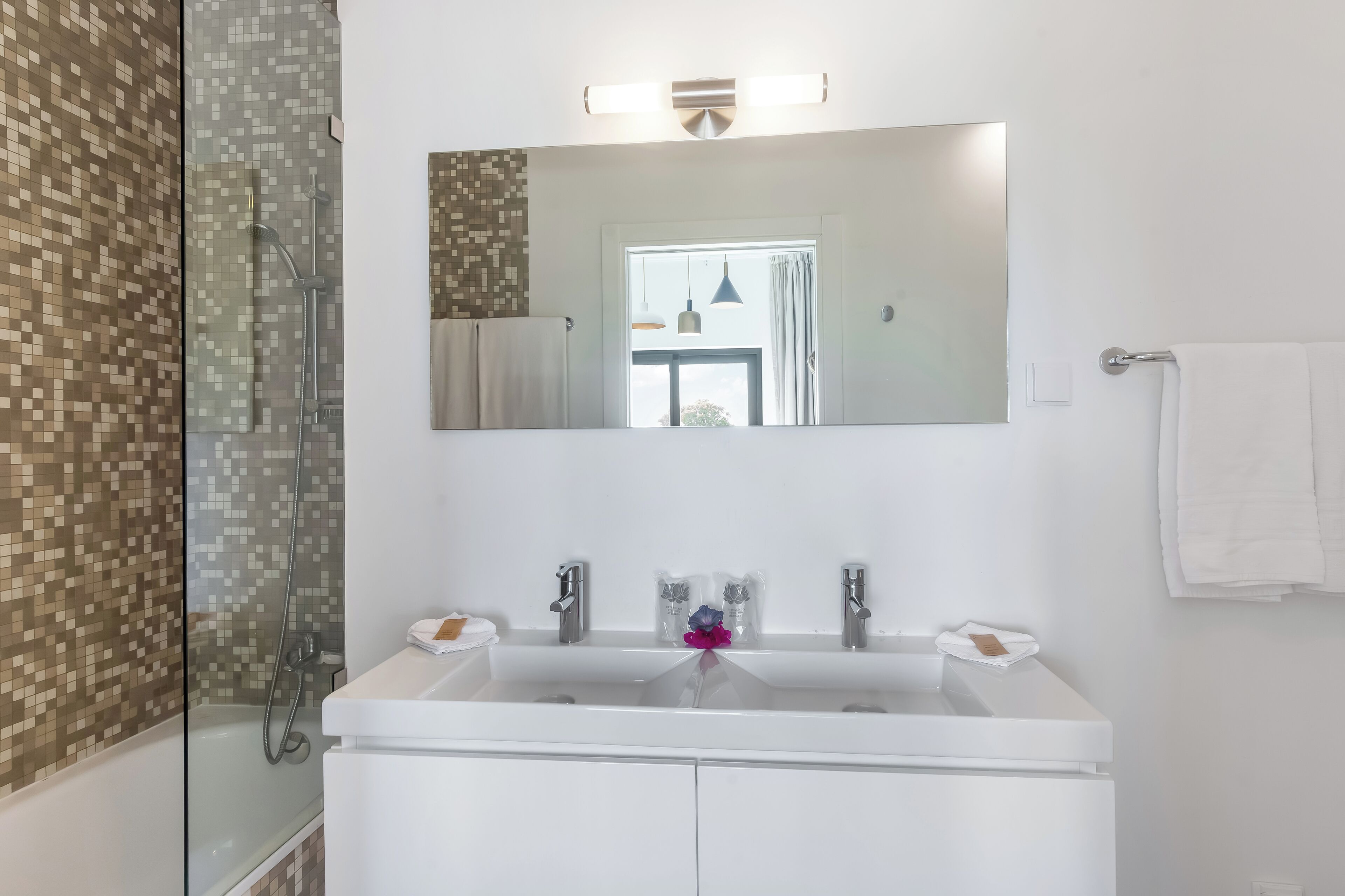 Een moderne badkamer met een grote spiegel, een wit wastafelmeubel en een douchecabine met glazen wanden.