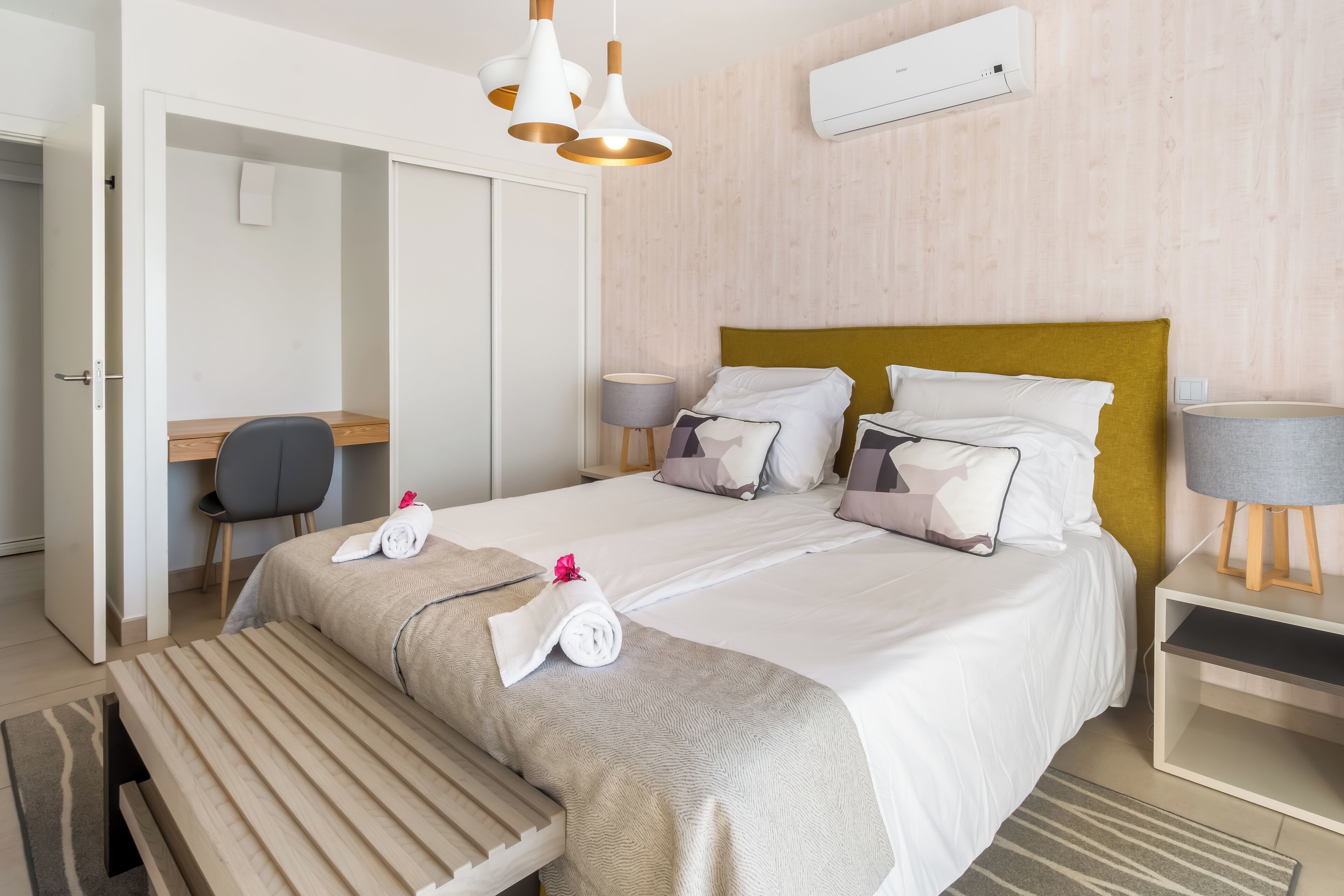 Una habitación de hotel con cama, mesitas de noche, escritorio, silla y banco.
