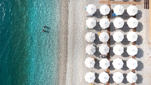 Vista aérea de una playa con sombrillas blancas y sillas de descanso dispuestas en filas.