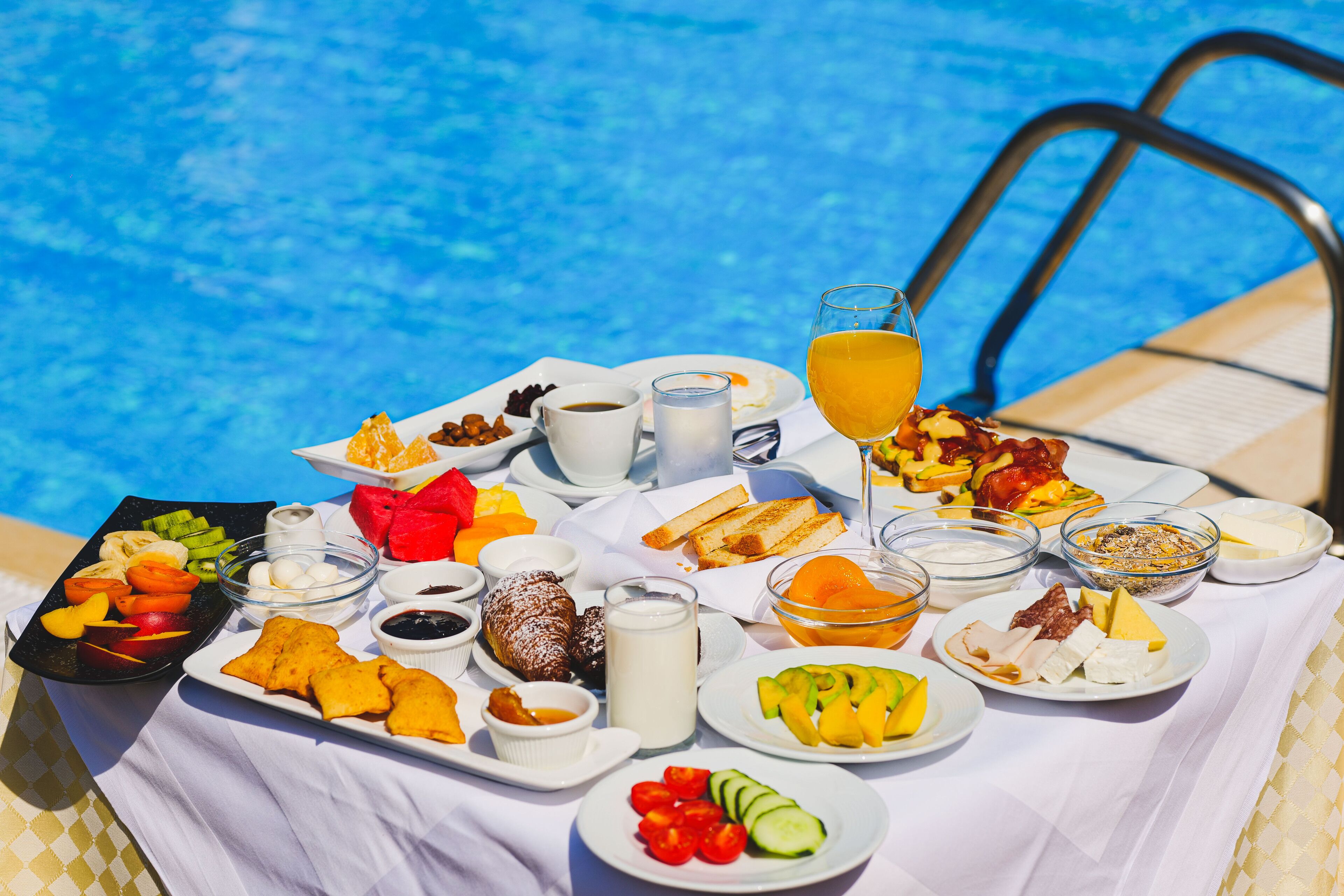 Een ontbijtbuffet bij een zwembad, met verschillende soorten eten en drinken.
