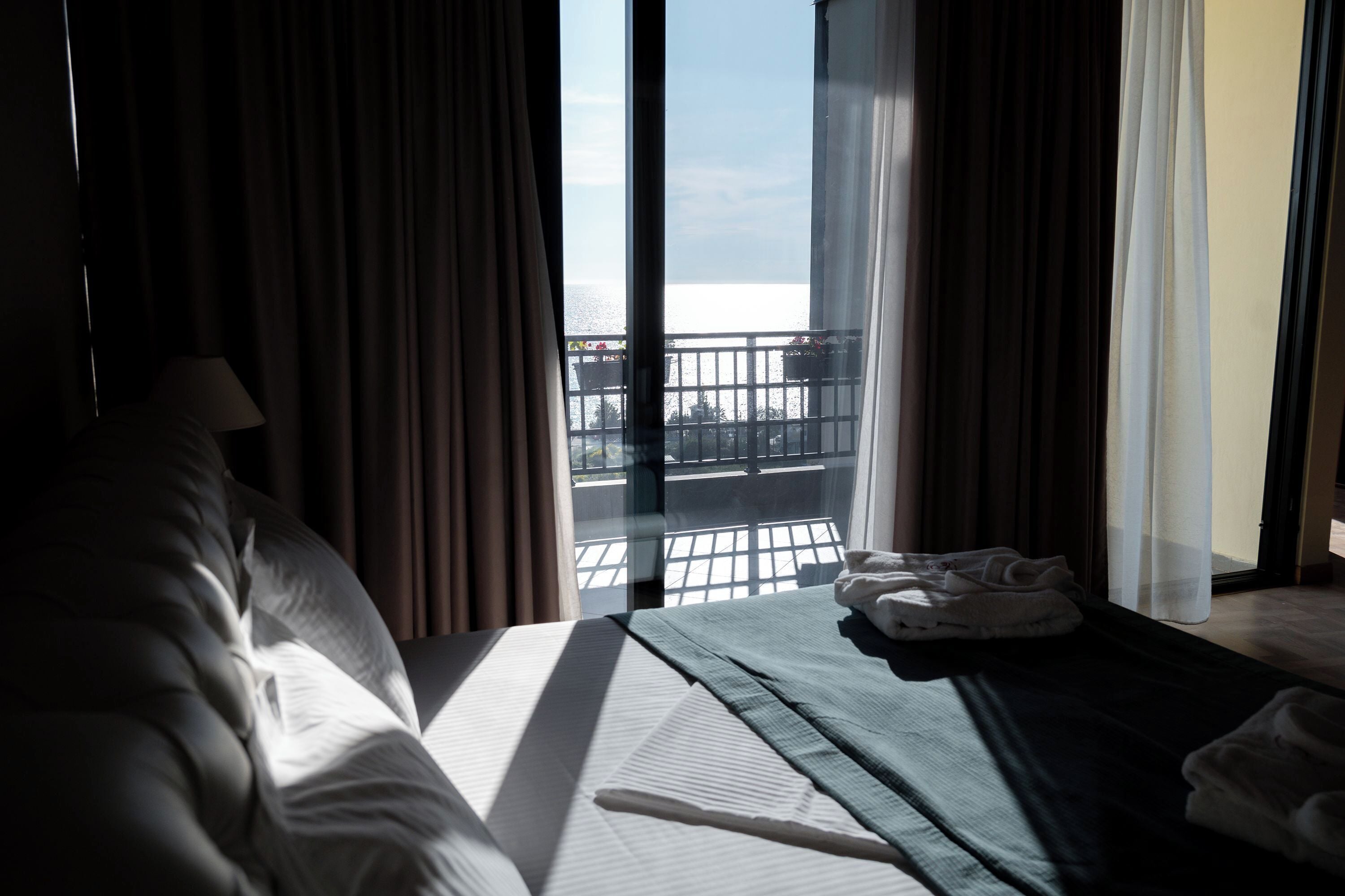 A hotel room with a bed, a window with curtains, and a view of the sea.
