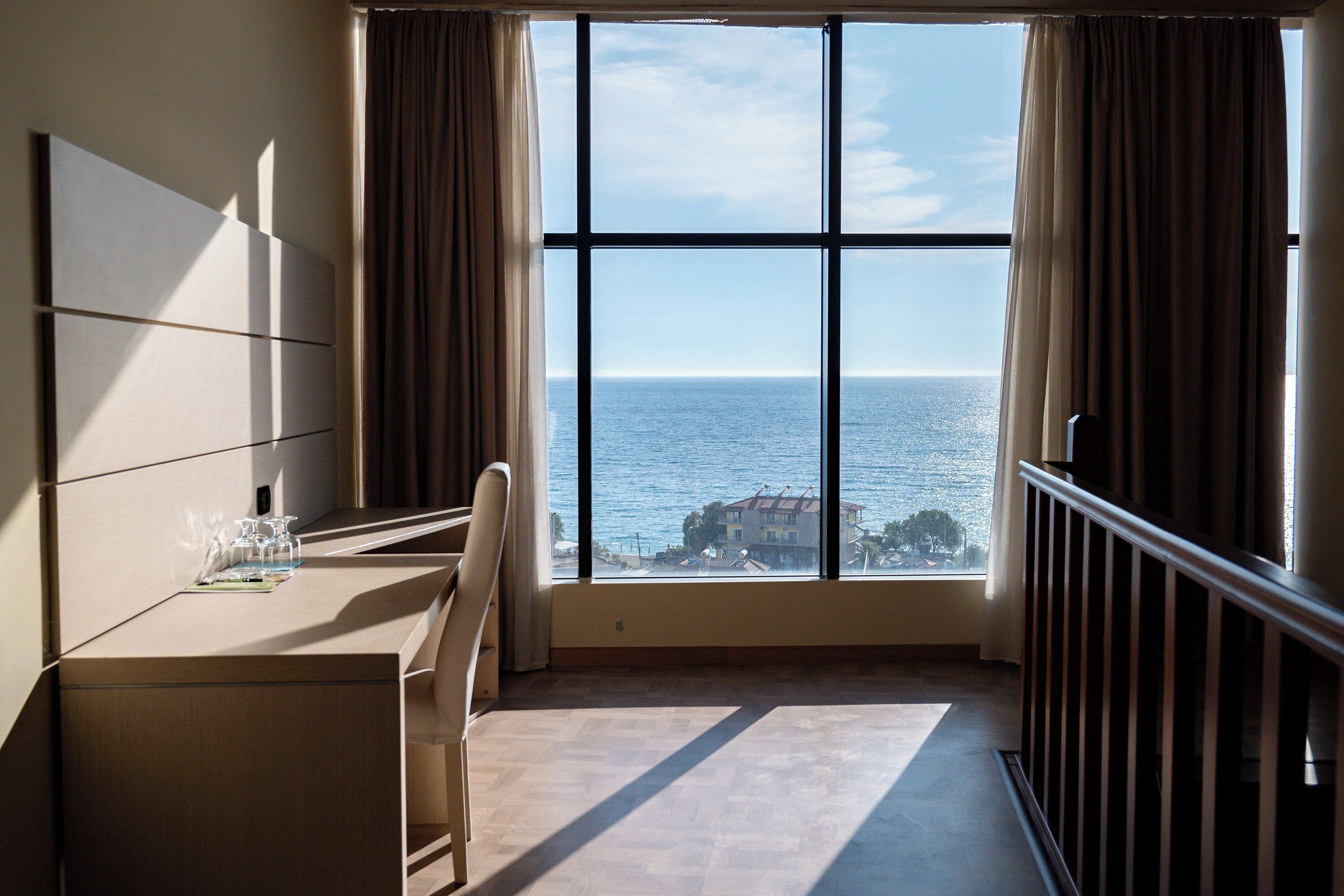 Ein Hotelzimmer mit großem Fenster, Schreibtisch und Stuhl.