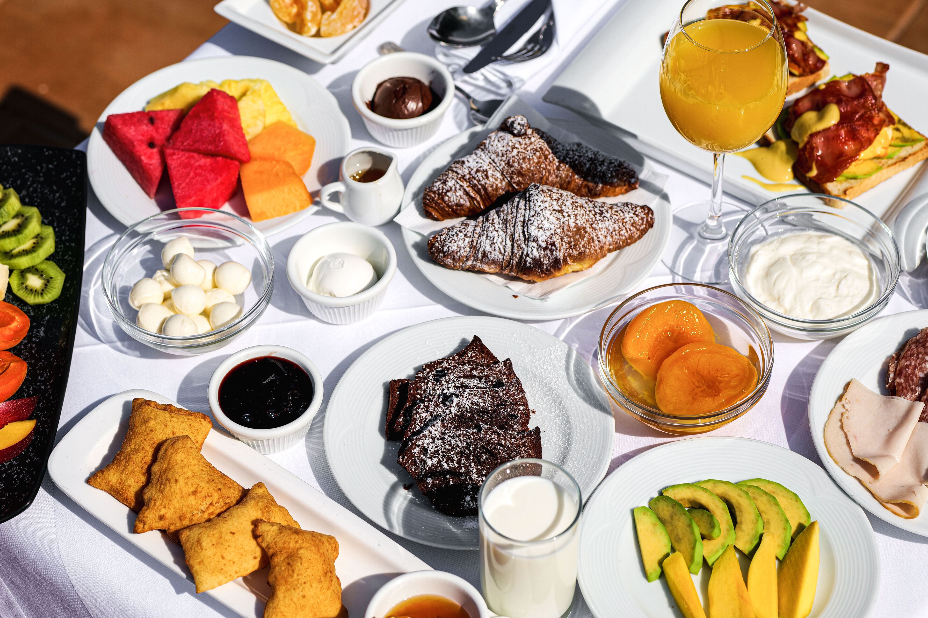 Una mesa con diversos productos para el desayuno, como bollería, frutas y bebidas.
