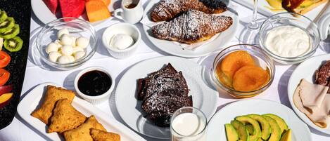 Una mesa con diversos productos para el desayuno, como bollería, frutas y bebidas.
