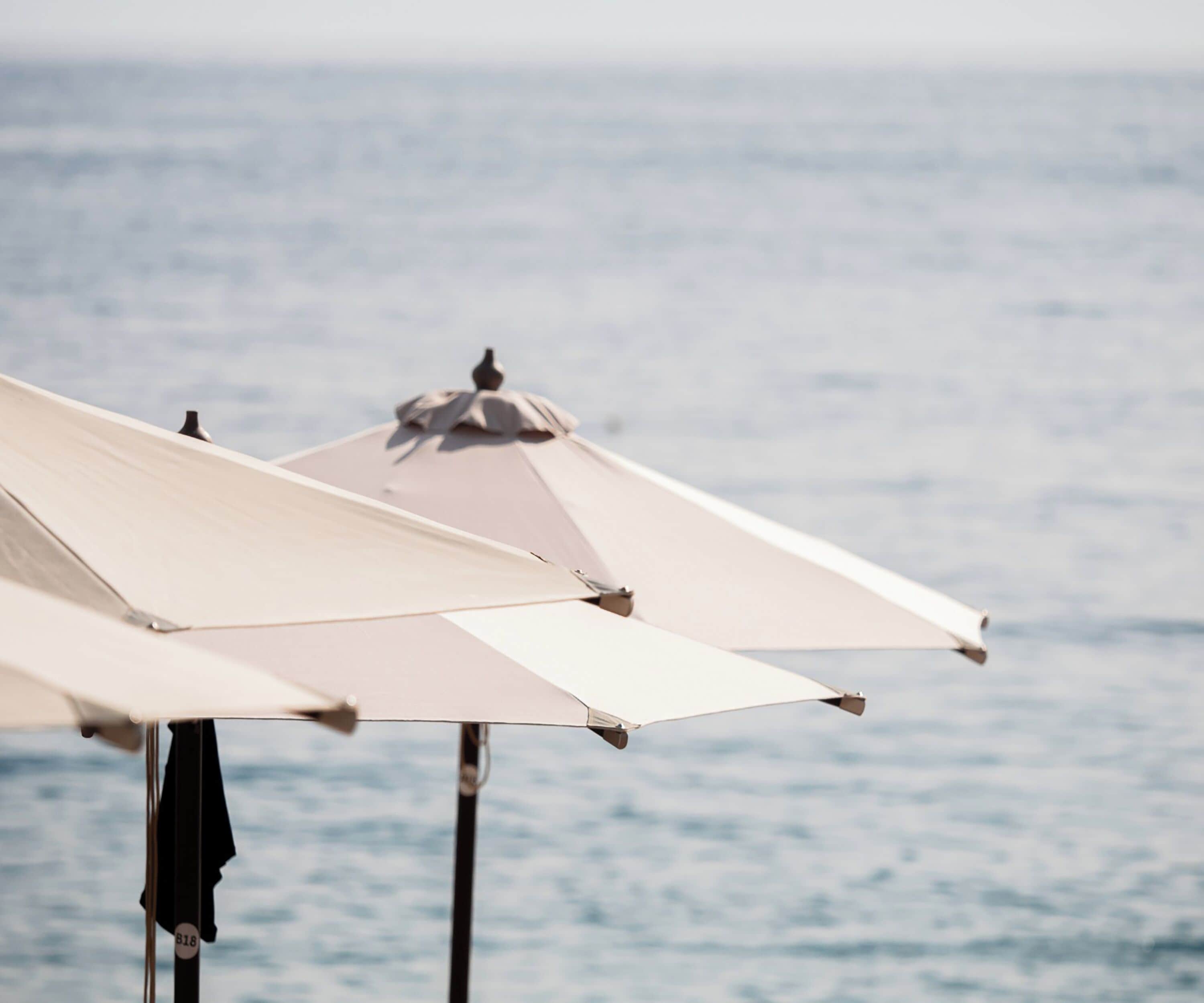 Un parasol de plage avec un oiseau perché dessus, le tout sur fond de mer.
