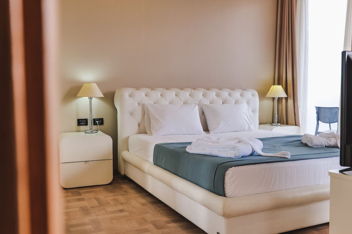 A neatly made bed with white linens and a green blanket, two bedside lamps, and a television on a stand.
