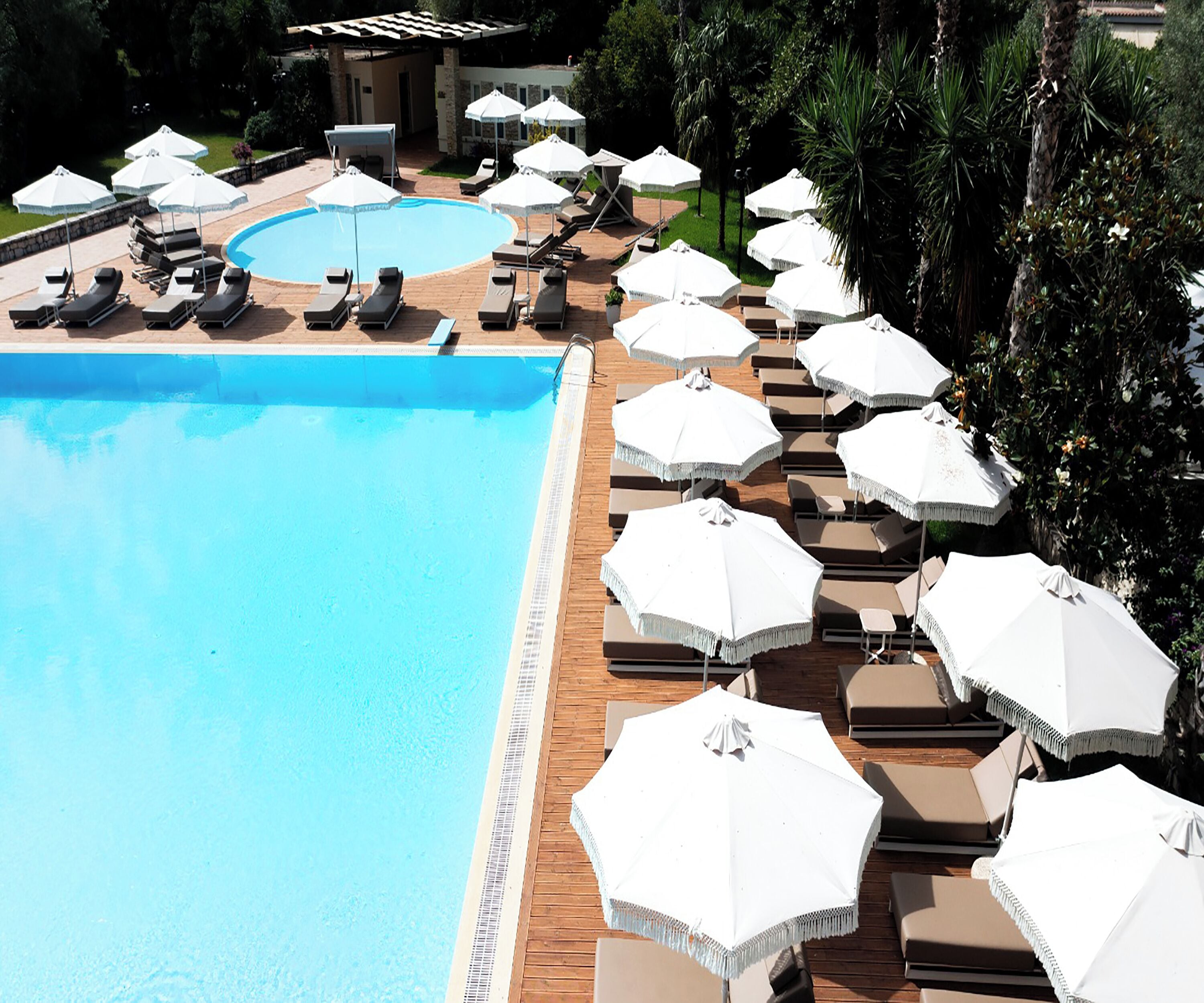 A poolside area with lounge chairs and umbrellas, a smaller pool, and a building in the background.