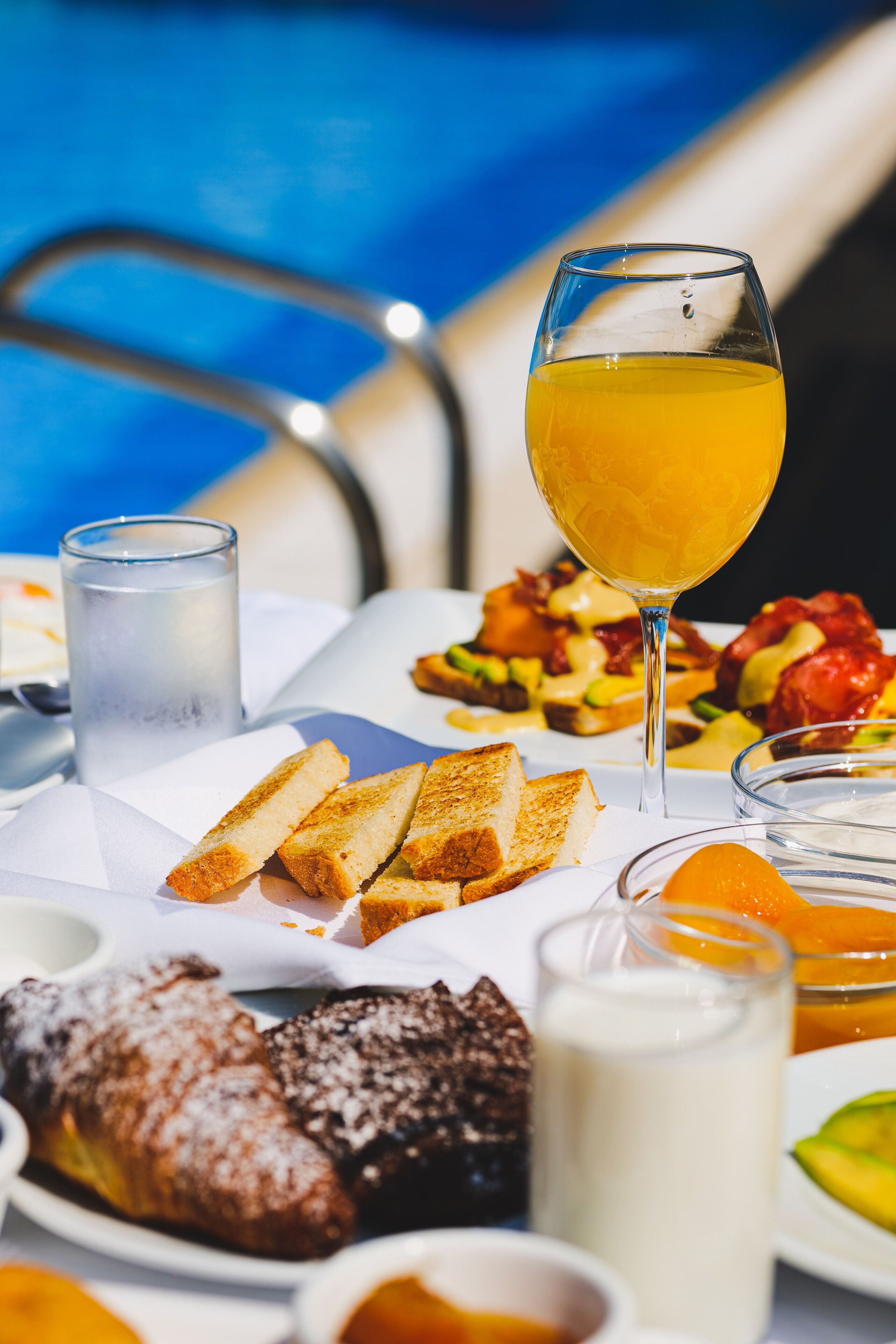Une table dressée pour le petit-déjeuner avec des toasts, des croissants, des fruits et un verre de jus d’orange.