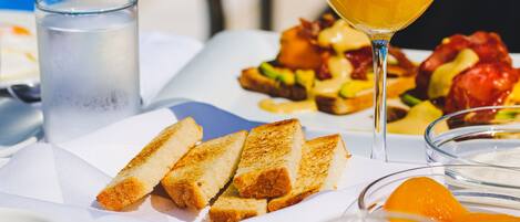 Une table dressée pour le petit-déjeuner avec des toasts, des croissants, des fruits et un verre de jus d’orange.