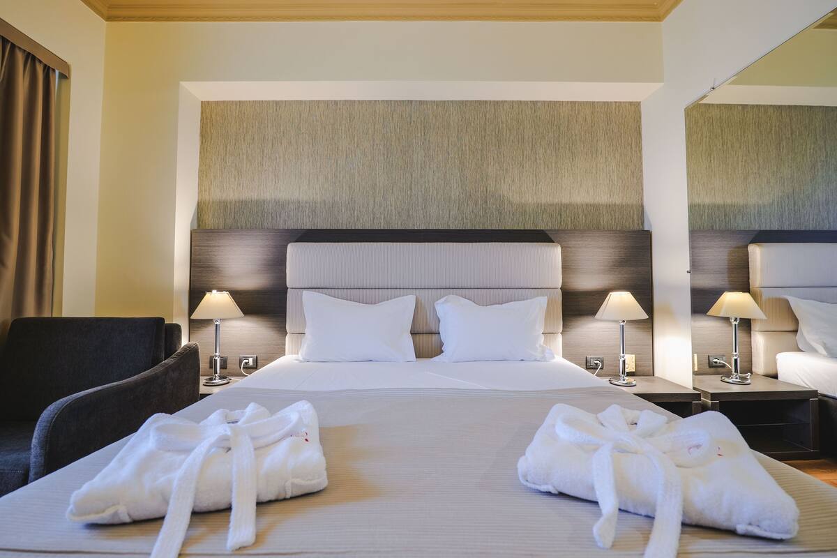 A hotel room with a large bed, two bedside lamps, a chair, and two towels on the bed.