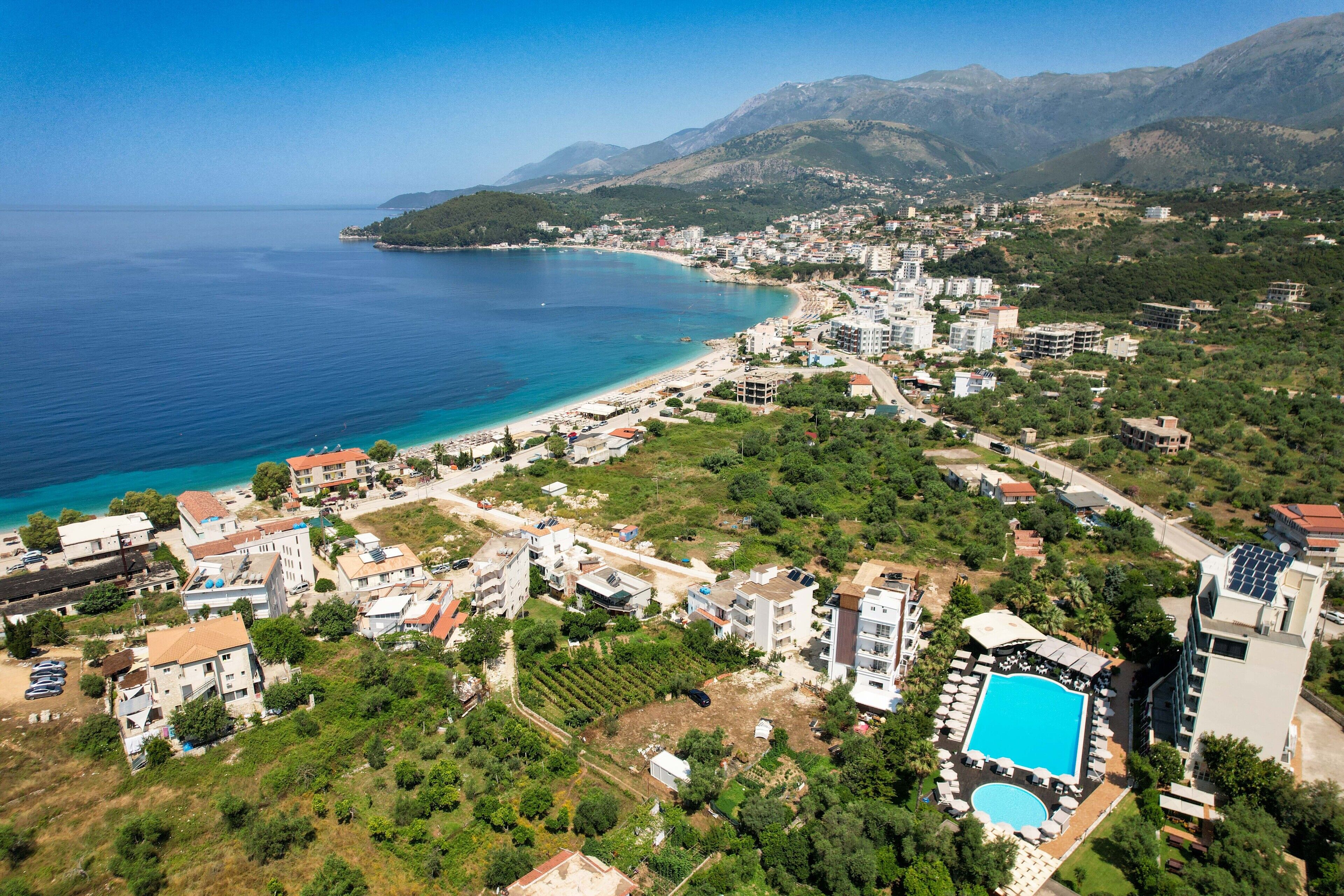 An aerial view of a coastal town with a beach, residential buildings, and a swimming pool.