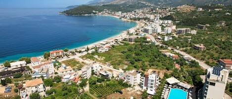 Vue aérienne d’une ville côtière avec une plage, des immeubles résidentiels et une piscine.