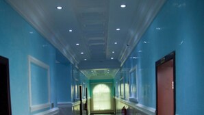 A hallway with blue walls, a marble floor, and a wooden door on the right. - Milestone Hotel Annex (Lekki)