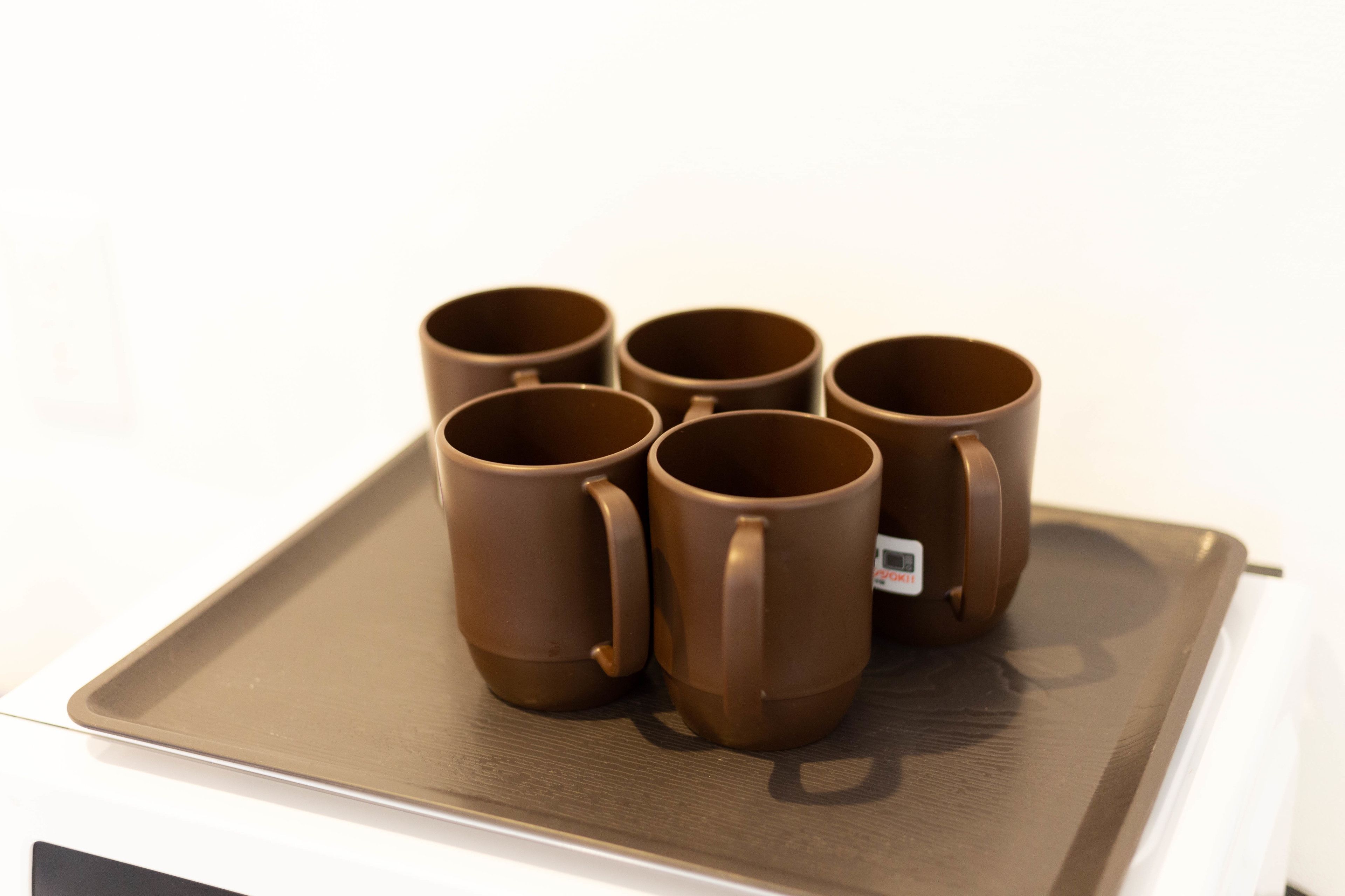 Un plateau sur lequel reposent six tasses brunes, posées sur une surface blanche.