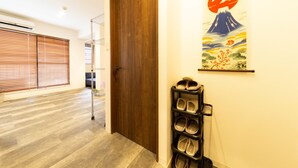 A hallway with a wooden door, a wall-mounted shelf with baskets, and a poster of Mount Fuji. - Guest House Megu-chan (Osaka)