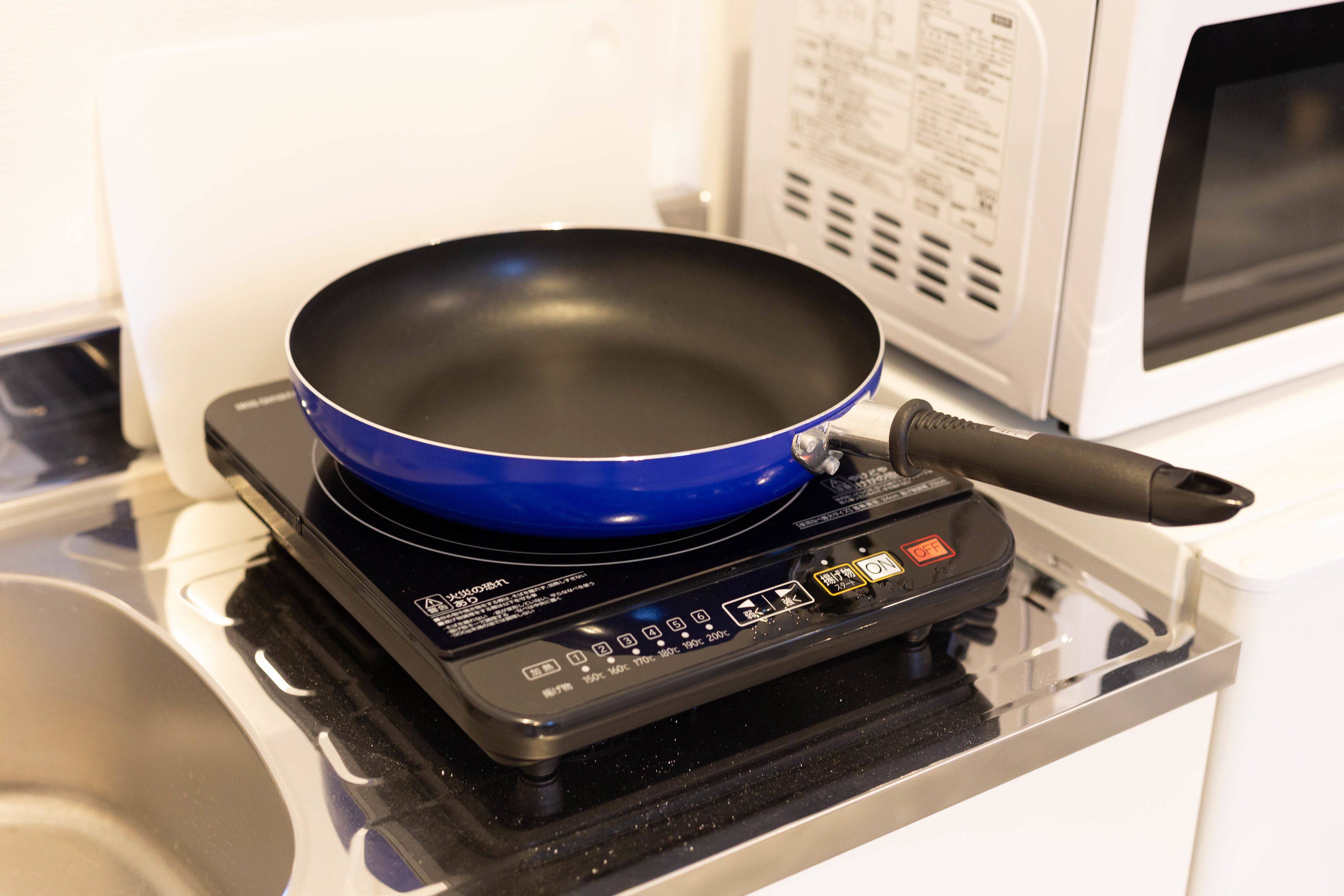 A portable electric stove with a blue frying pan on it, placed on a glass countertop.