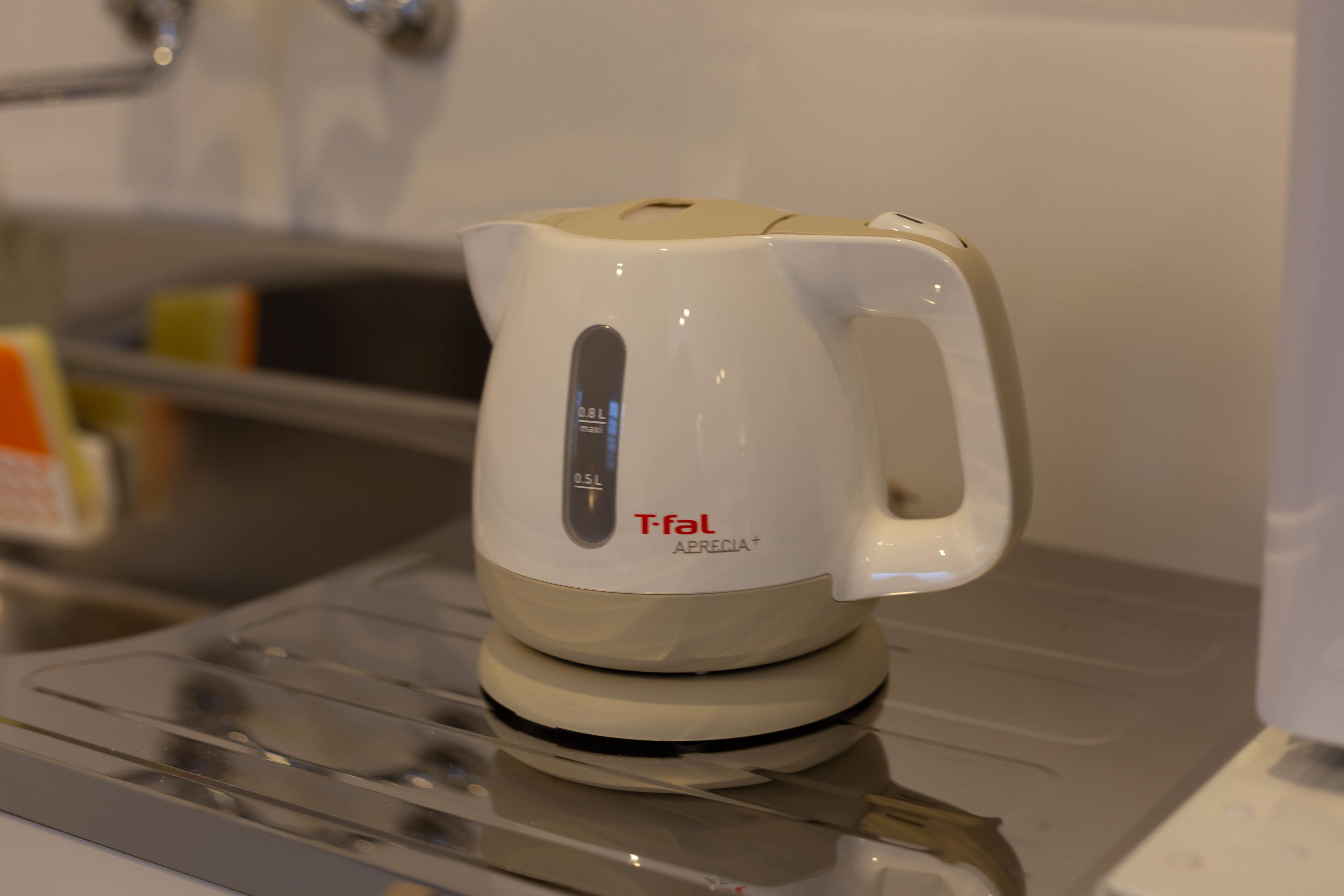 Una tetera eléctrica blanca con un asa y una pantalla digital sobre una encimera de cocina.