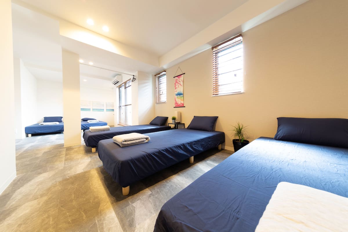 A hotel room with three beds, a small table, and a potted plant.