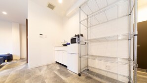 A modern kitchen with white cabinets, a microwave, and a wire shelving unit. - Guest House Megu-chan (Osaka)