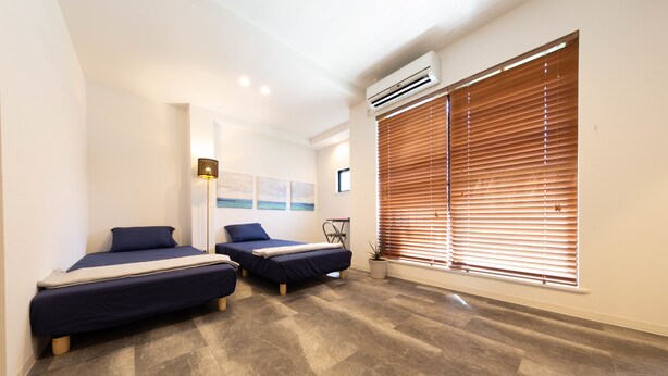 A modern bedroom with two beds, a potted plant, and a large window with blinds. - Guest House Megu-chan (Osaka)