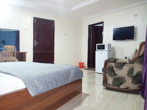 Una habitación de hotel con una cama, una silla, un televisor, un microondas y una puerta.