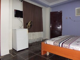 A bedroom with a bed, a white wardrobe, a television mounted on the wall, a fan, and a door.