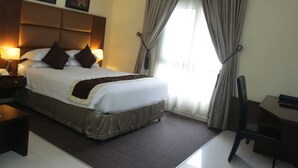 A hotel room with a large bed, bedside lamps, a desk, and a chair. - Olive Branch Hotel (Port Harcourt)