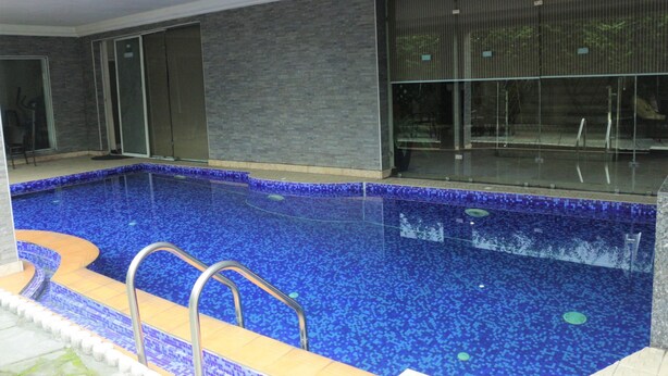 An indoor swimming pool with a blue mosaic tile floor, a metal ladder, and a glass enclosure. - Olive Branch Hotel (Port Harcourt)