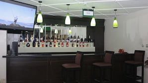 A bar area with a long counter displaying various bottles, three bar stools, and hanging green pendant lights. - Olive Branch Hotel (Port Harcourt)