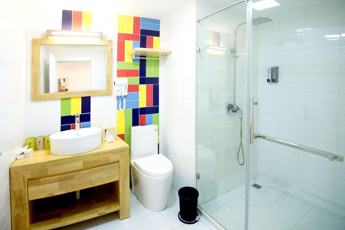 A modern bathroom with a wooden vanity, a white sink, a toilet, and a glass-enclosed shower.