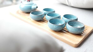Una bandeja de madera con seis tazas de cerámica azules y una tetera.
