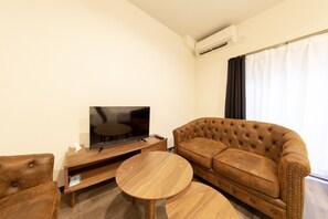 A living room with a flat-screen TV, a brown leather sofa, a wooden coffee table, and a wooden TV stand. - Guest House ICHIKA (Kyoto)