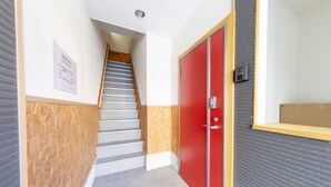 A hallway with a staircase, a red door, and a sign on the wall. - Guest House ICHIKA (Kyoto)