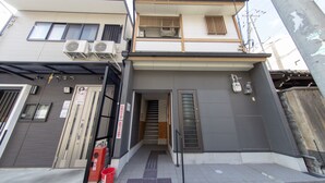 A two-story building with a ground-floor entrance, a staircase, and a red fire extinguisher. - Guest House ICHIKA (Kyoto)