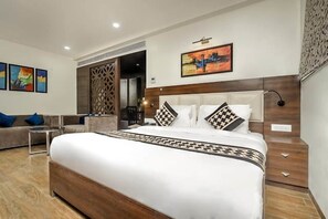 A modern hotel room with a large bed, a sofa, a small table, and artwork on the walls. - JB Skyhilton Inn (Lucknow)