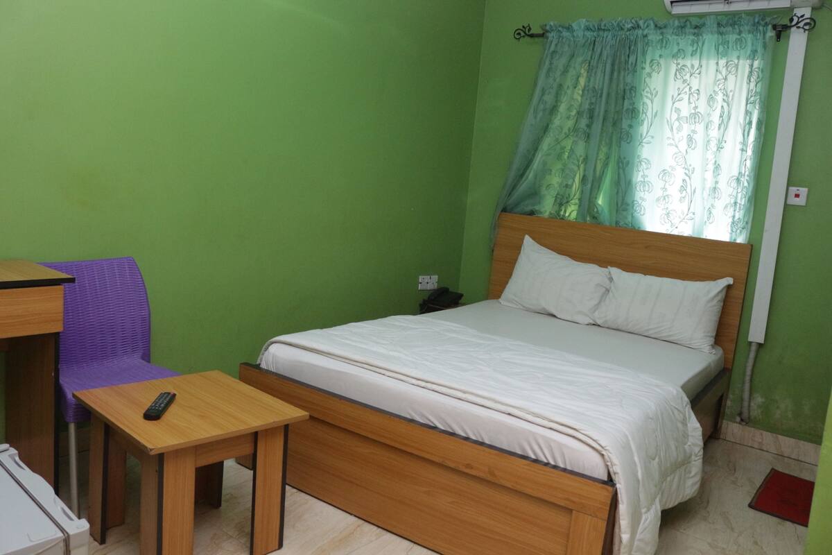 A room with a bed, a small table, a chair, and a window with a curtain.