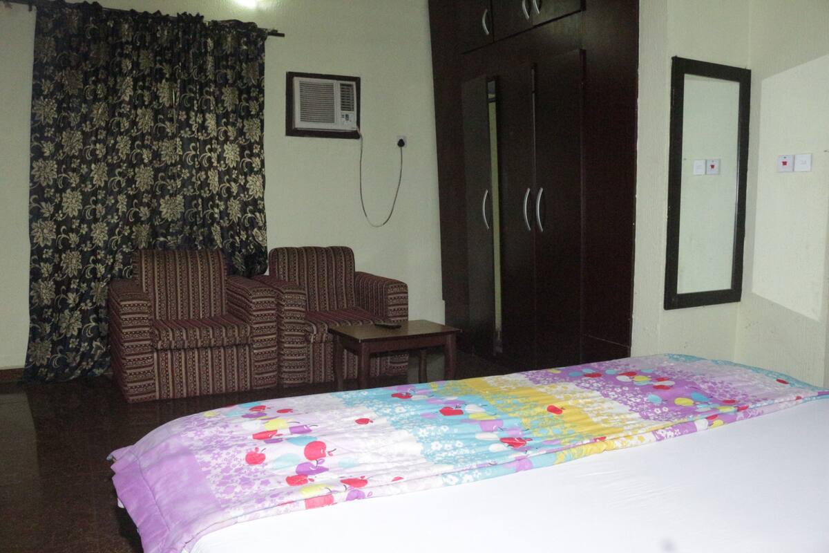 A bedroom with a bed, a sofa, a small table, and a wardrobe.