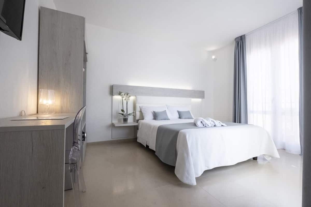 A modern hotel room with a bed, bedside table, and a TV mounted on the wall.