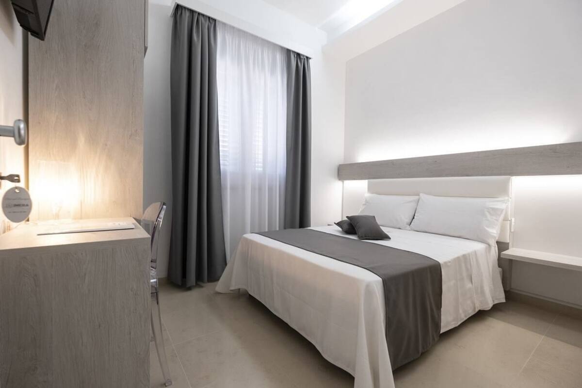 A hotel room with a bed, a desk, a chair, and a window with curtains.