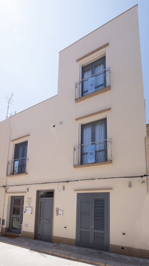 A multi-story building with balconies, a door with a sign, and a window with a curtain. - Imera B&B (Favignana)